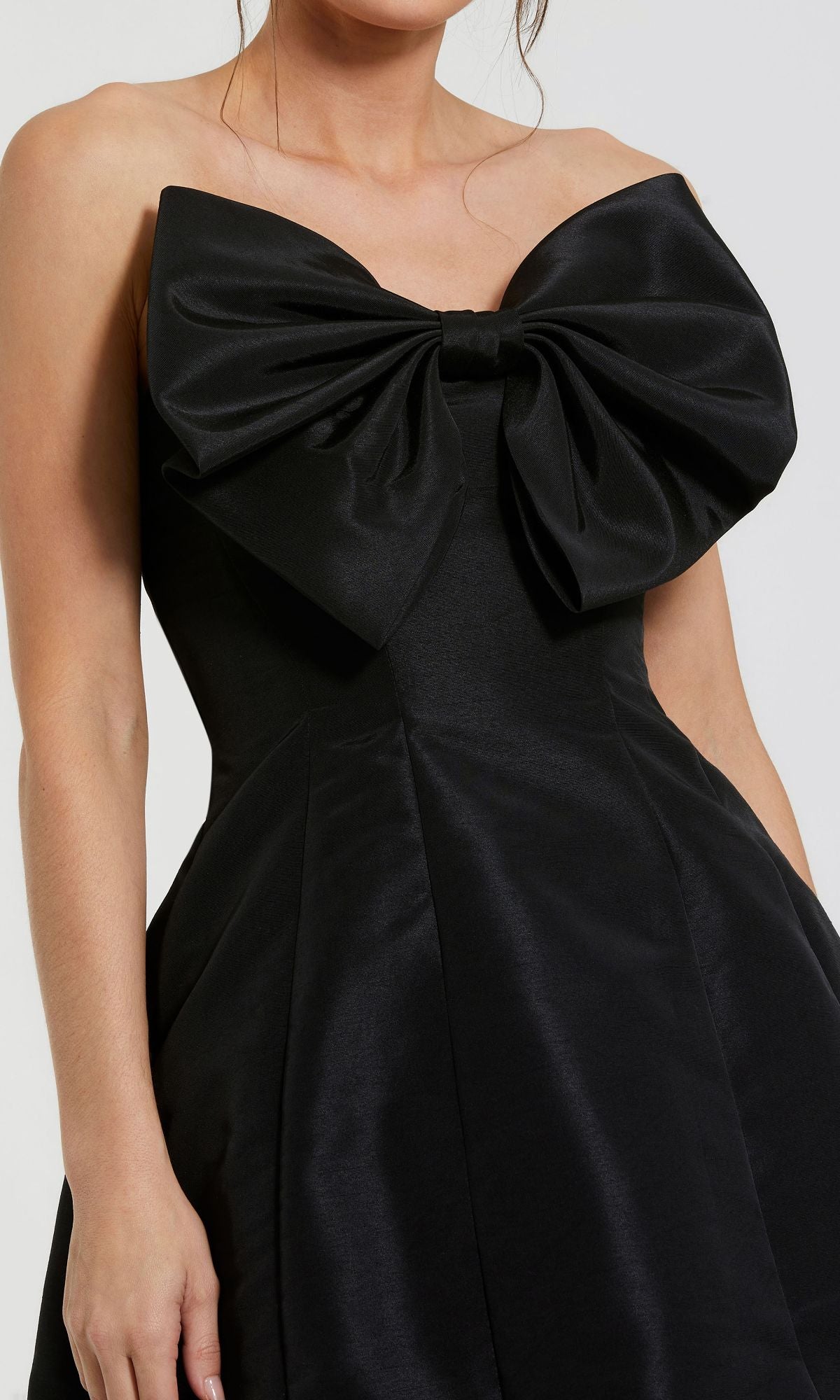 A woman wears the Mac Duggal 49210 Strapless Short Bow Party Dress, shown from shoulders to hips, featuring a front bow detail.